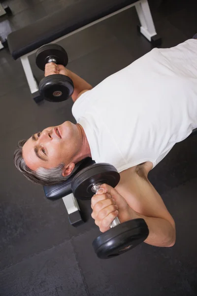 Fit man lifting dumbbells lying on the bench — Stock Photo, Image