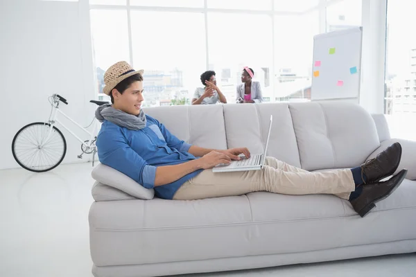 Joven hombre creativo utilizando el ordenador portátil en el sofá —  Fotos de Stock