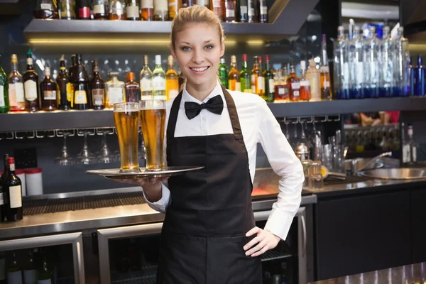 Kellnerin mit einer Hand auf der Hüfte, die ein Tablett Champagner hält — Stockfoto