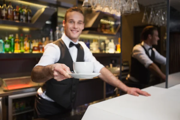 Garçom sorrindo oferecendo xícara de café sorrindo para a câmera — Fotografia de Stock