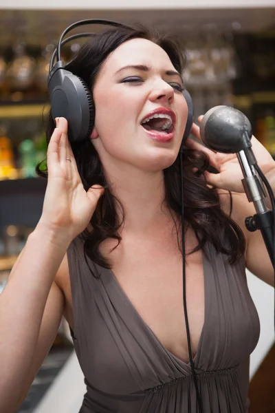 Kobieta śpiewa z jej ręce na jej wyjście słuchawkowe — Zdjęcie stockowe