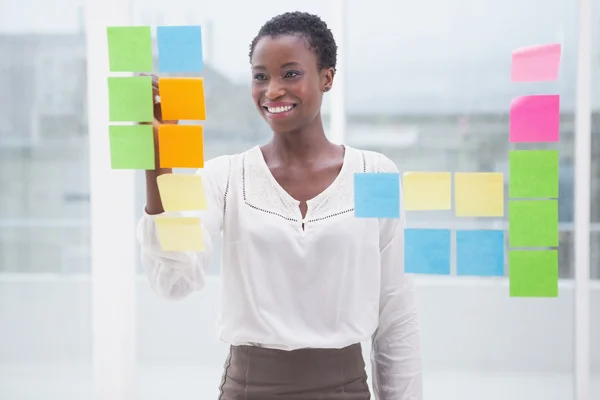 Smiling businesswoman writing on sticky notes on window — Stock Photo, Image