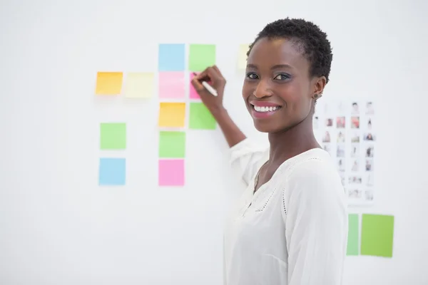 Diseñador sonriente escribiendo en notas adhesivas y mirando a la cámara — Foto de Stock