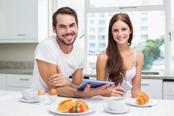 年轻的夫妇在吃早饭时使用平板电脑 — 图库照片