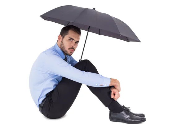 Unsmiling businessman holding umbrella sitting on the floor — Stock Photo, Image