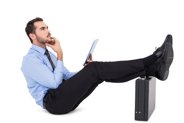 Uomo d'affari seduto con i piedi sulla sua valigetta pensando — Foto Stock
