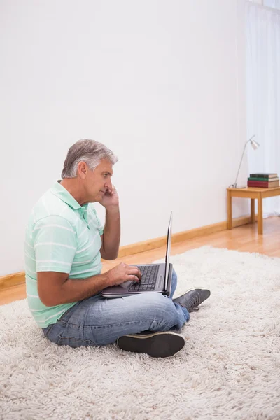 Mature man sitting on rug using laptop — Stock Photo, Image