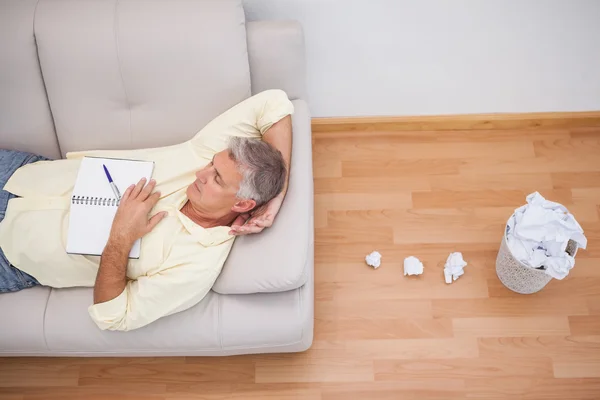Man lying on couch with crumpled papers — Stock Photo, Image
