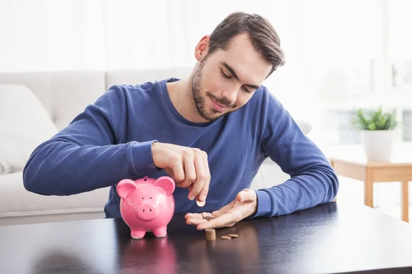 Jonge man munten aanbrengend piggy bank — Stockfoto