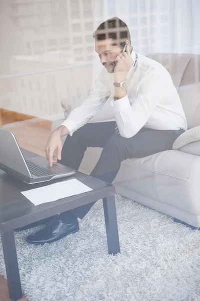 Empresario trabajando en su sofá visto a través del vidrio — Foto de Stock