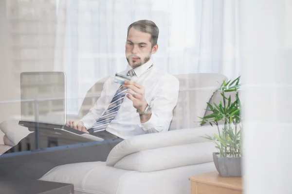 Zakenman online winkelen op zijn bank gezien door glas — Stockfoto