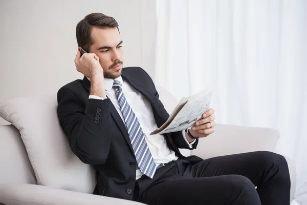 Affärsman att ringa på hans soffa läser tidningen — Stockfoto