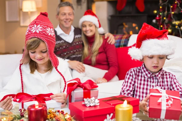 Праздничные маленькие братья и сёстры открывают подарок перед родителями — стоковое фото