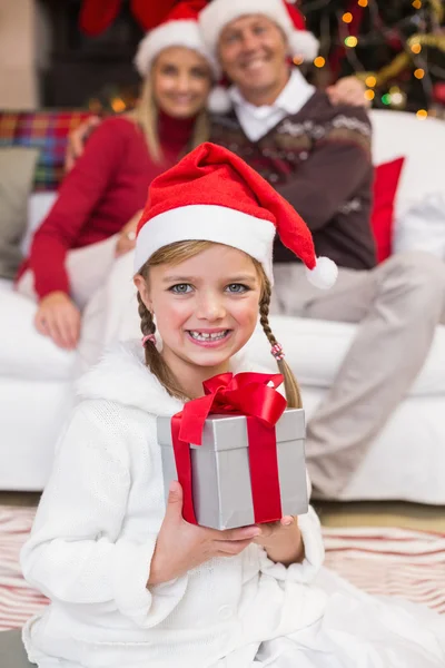 Niña sonriente sosteniendo un regalo con sus padres detrás —  Fotos de Stock