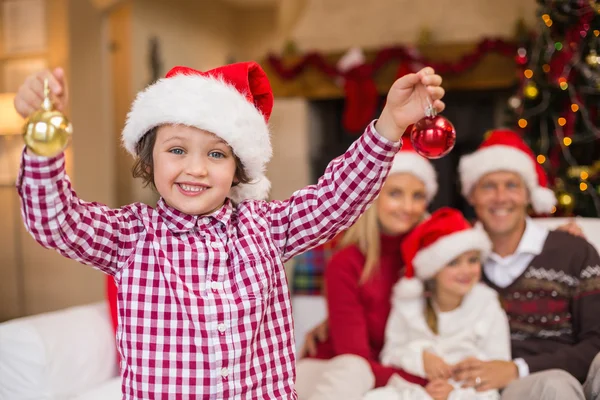 儿子穿着圣诞老人的帽子，拿着在他家人面前的小玩意 — 图库照片