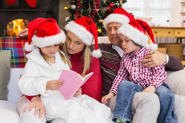 Família festiva vestindo chapéu de Papai Noel enquanto lê no sofá — Fotografia de Stock