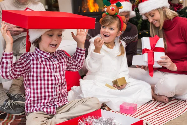 Fils jouant avec un cadeau assis sur le sol avec sa famille — Photo