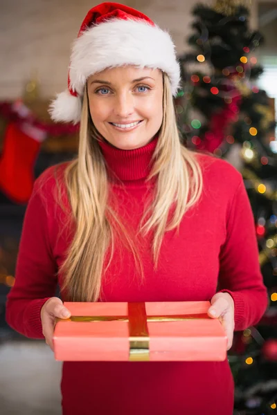 Mujer bonita en sombrero de santa sonriendo y sosteniendo un regalo —  Fotos de Stock