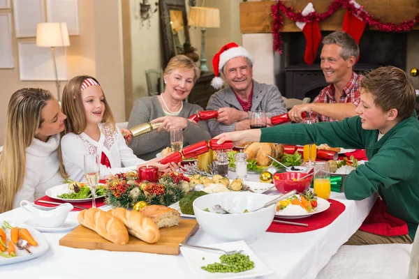 Smiling family pulling christmas crackers at the dinner table — Stock Photo, Image