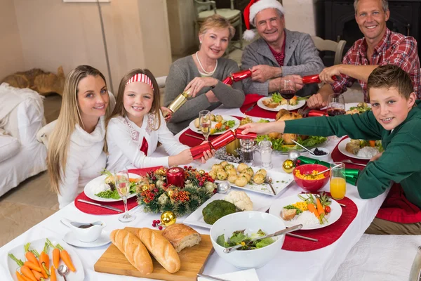 Smiling family pulling christmas crackers at the dinner table — Stock Photo, Image