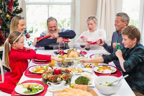 Family pulling christmas crackers at the dinner table — Stock Photo, Image