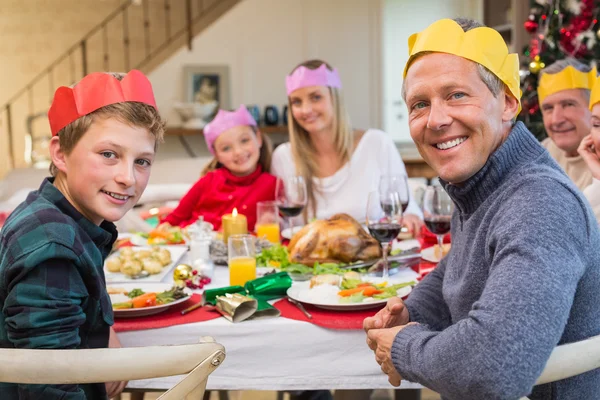 Sonriente familia extendida en sombrero de fiesta en la mesa de la cena —  Fotos de Stock