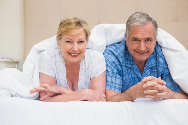 Pareja mayor sonriendo bajo el edredón — Foto de Stock