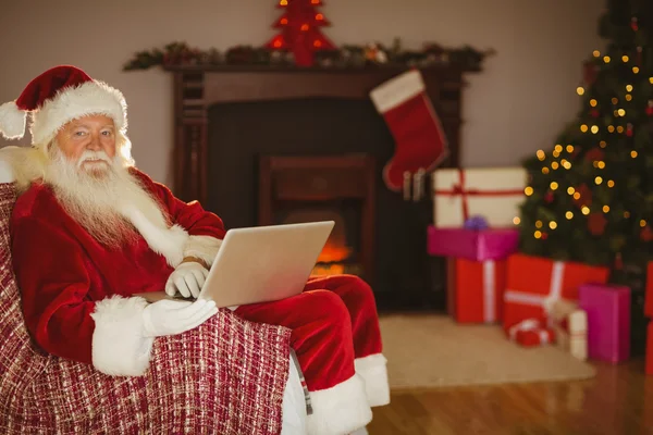 圣诞老人在圣诞节在沙发上使用笔记本电脑 — 图库照片