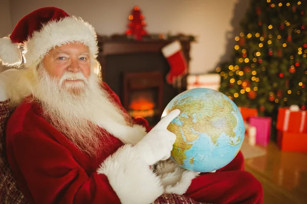 Smiling santa pointing his finger on the globe — Stock Photo, Image