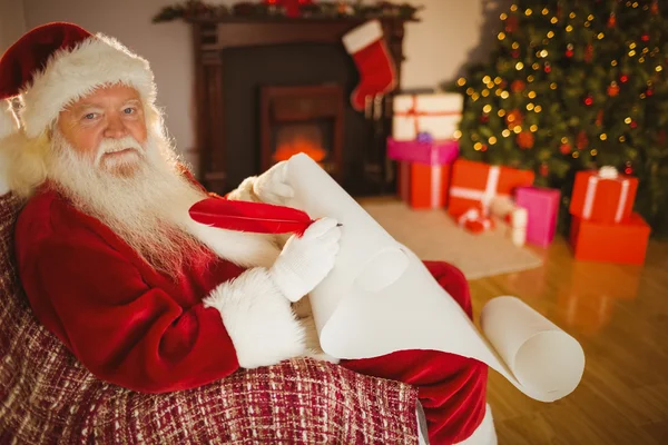 Smiling santa claus writing his list on scroll — Stock Photo, Image