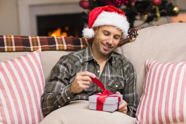 Glimlachende man in Kerstman hoed openen een geschenk — Stockfoto