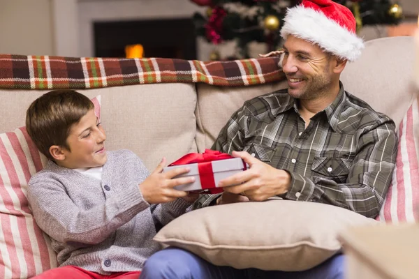 Son att ge pappa en julklapp på soffan — Stockfoto