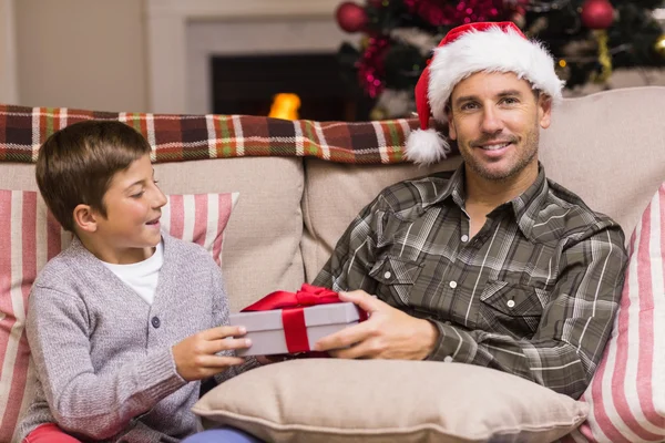 Filho dando ao pai um presente de Natal no sofá — Fotografia de Stock