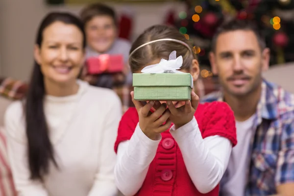 Tochter zeigt ein Geschenk mit ihrer Familie im Rücken — Stockfoto
