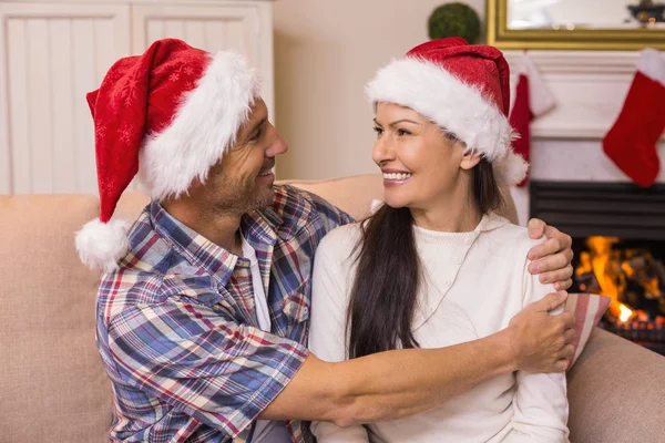 Festive couple in santa hat hugging on the couch — Stock Photo, Image