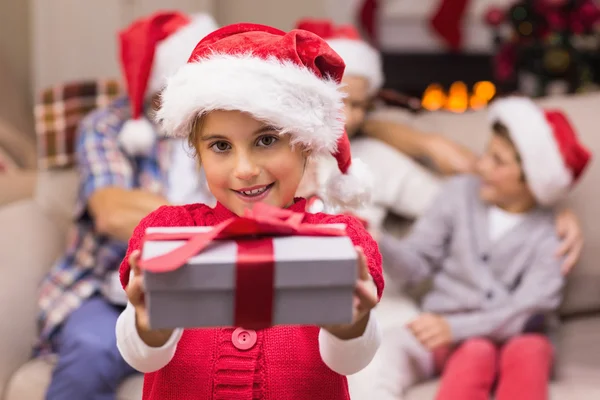 Smiling little girl offering a gift with her parents behind Stock Photo