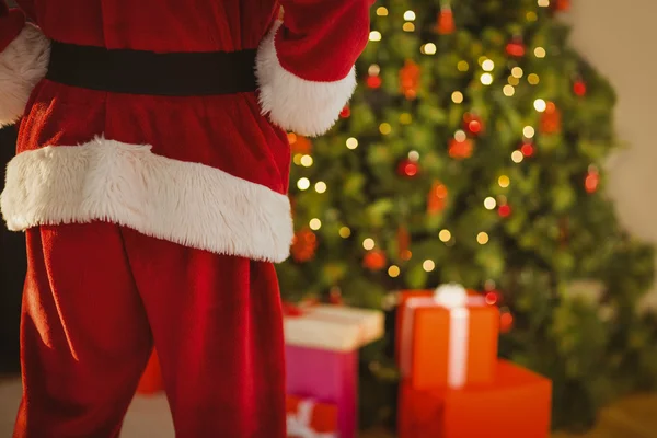 Mid section of santa standing in front of the christmas tree — Stock Photo, Image