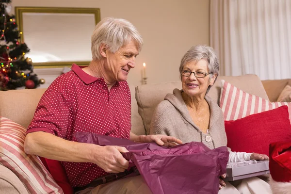 Senior couple opening a christmas present on sofa — Stock Photo, Image