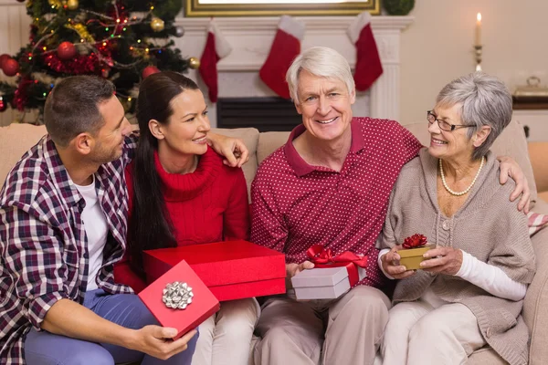 Smiling family holding gift on sofa — Stock Photo, Image