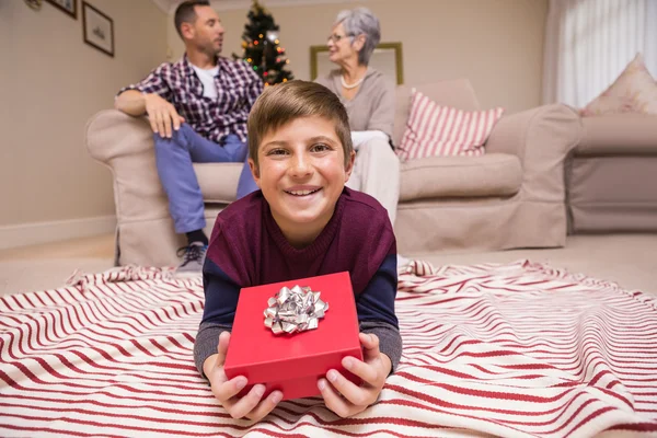 Feliz hijo mintiendo y sosteniendo regalo con su familia detrás —  Fotos de Stock