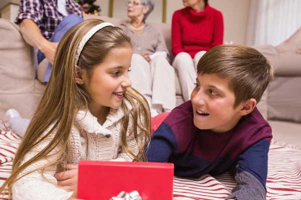 Smiling brother and sister lying and opening gift — Stock Photo, Image