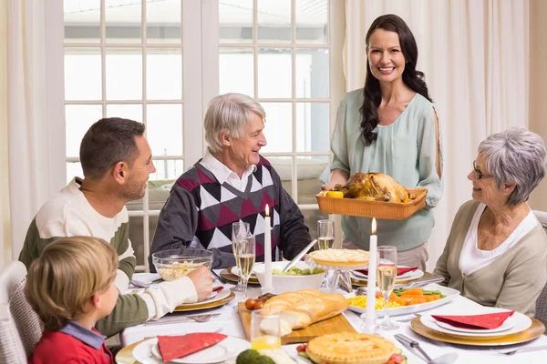 Mujer sosteniendo pavo asado con la familia en la mesa de comedor —  Fotos de Stock