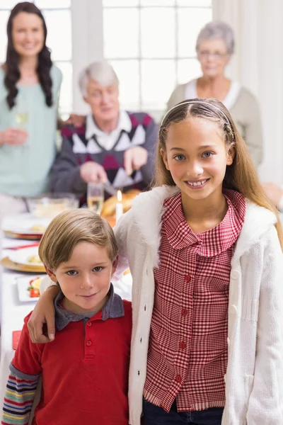 Hermano y hermana sonriendo a la cámara delante de su familia — Foto de Stock