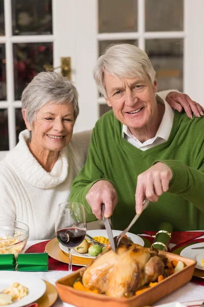 Man carving chicken while his wife having arm around him — Stock Photo, Image