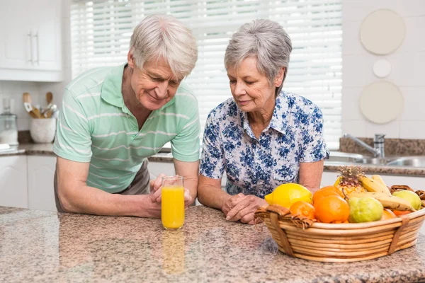 Casal sênior olhando para o vidro de suco de laranja — Fotografia de Stock