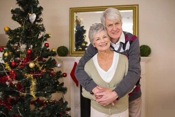 Senior paar knuffelen naast hun kerstboom — Stockfoto