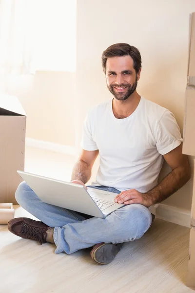 Happy man using laptop surrounded by boxes — Stock Photo, Image