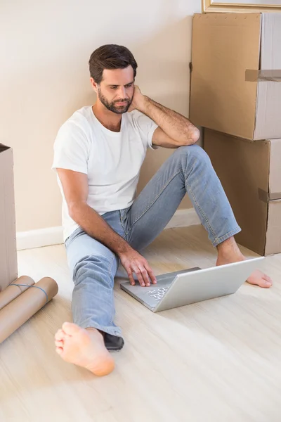 Happy man using laptop surrounded by boxes — Stock Photo, Image