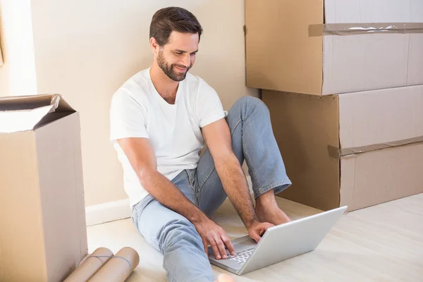 Happy man using laptop surrounded by boxes — Stock Photo, Image