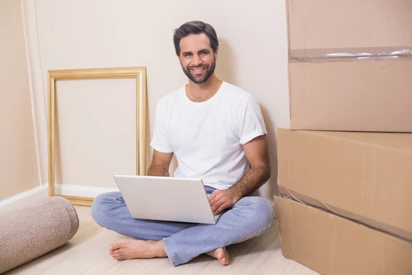 Happy man using laptop surrounded by boxes — Stock Photo, Image